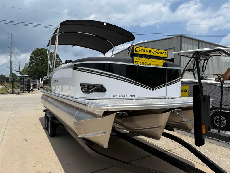 Slide: The Image of 2025 Avalon LSZ Versatile Rear Bench pontoon boat on trailer, outdoor display. - 2