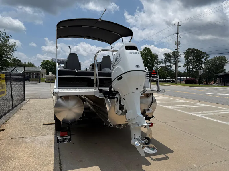 Slide: The Image of 2025 Avalon LSZ Versatile Rear Bench pontoon boat with outboard motor, parked on pavement. - 5