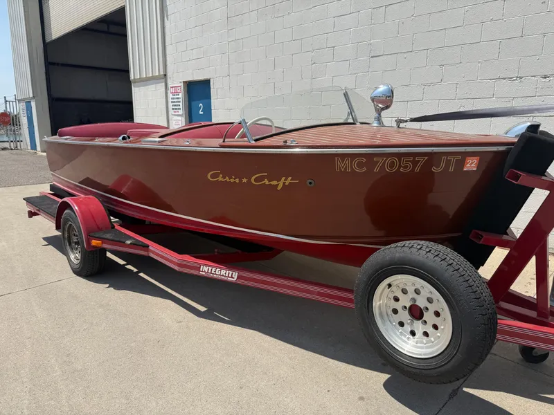 The Image of 1953 Chris-Craft 17’ Sportsman boat on trailer, parked outside a building. - 0