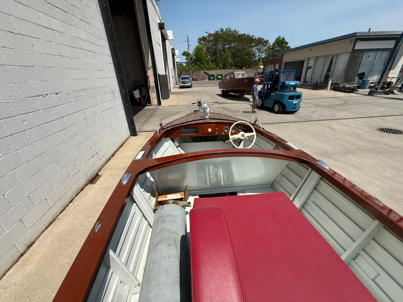 Slide: The Image of 1953 Chris-Craft 17’ Sportsman boat with red interior, parked outdoors near industrial buildings. - 7