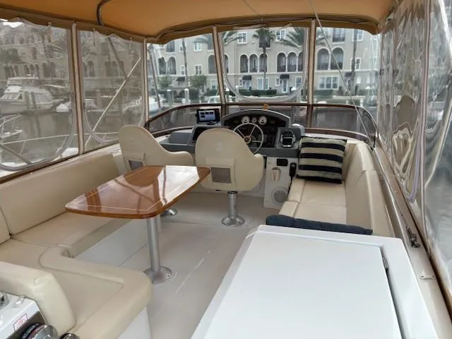 Slide: The Image of 2014 Beneteau Swift Trawler 44 interior with seating, table, and helm in marina setting. - 3