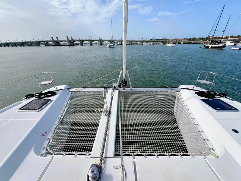 Slide: The Image of 2024 Lagoon 42 catamaran with netted deck, anchored in a serene harbor. - 13