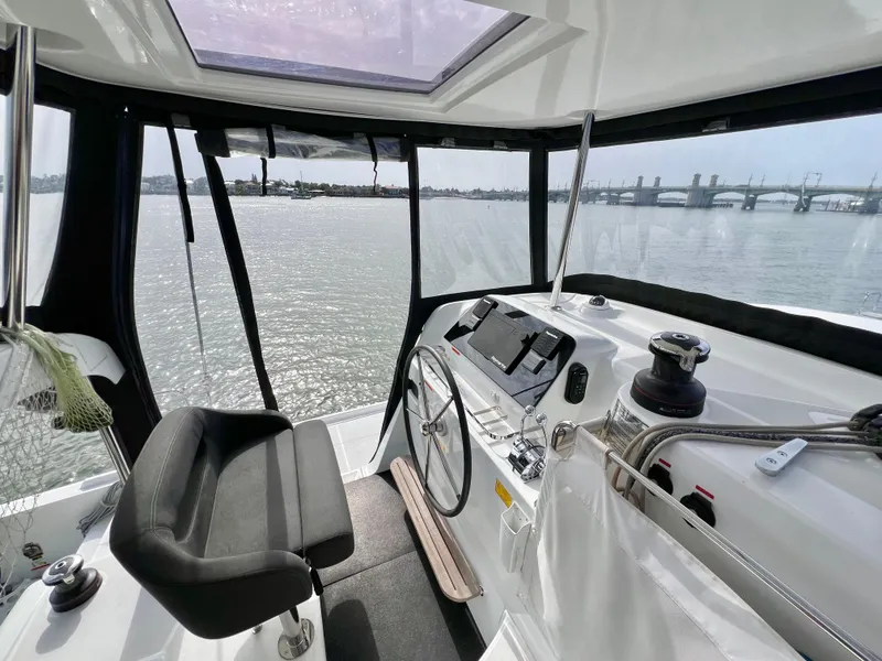 Slide: The Image of 2024 Lagoon 42 yacht cockpit with steering wheel, overlooking serene waters and distant bridge. - 28