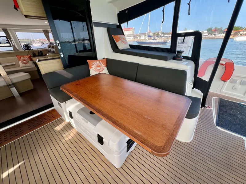 Slide: The Image of 2024 Lagoon 42 yacht interior with wooden table, cushioned seating, and marina view. - 33