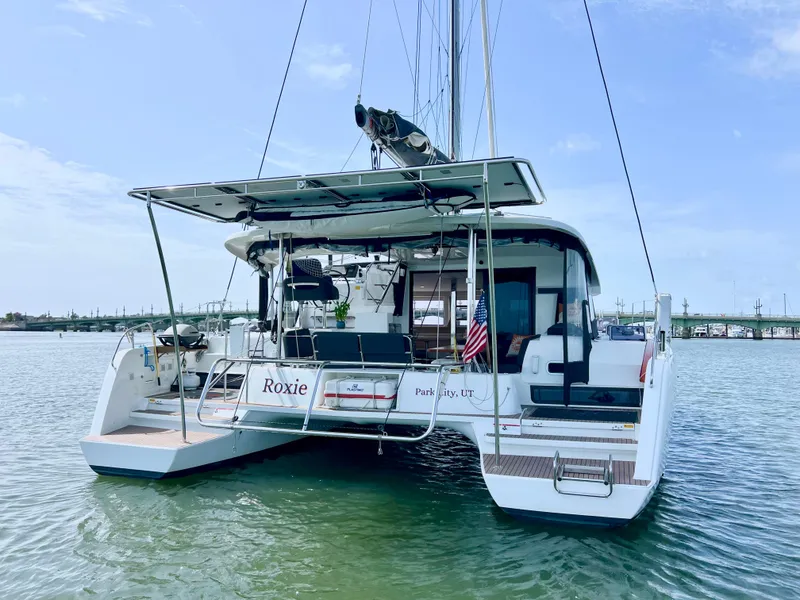 Slide: The Image of 2024 Lagoon 42 catamaran on water, rear view, with American flag and clear sky. - 8