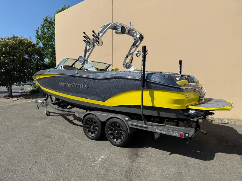 Slide: The Image of 2019 MasterCraft X22 boat in yellow and gray on a trailer, parked outdoors. - 2