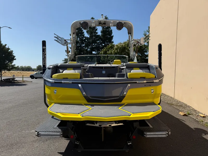 Slide: The Image of 2019 MasterCraft X22 boat, yellow and gray, rear view, parked outdoors. - 3