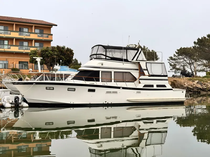 Slide: The Image of 1988 Overseas PT52 Cockpit Motoryacht docked near a building, reflecting on calm water. - 29