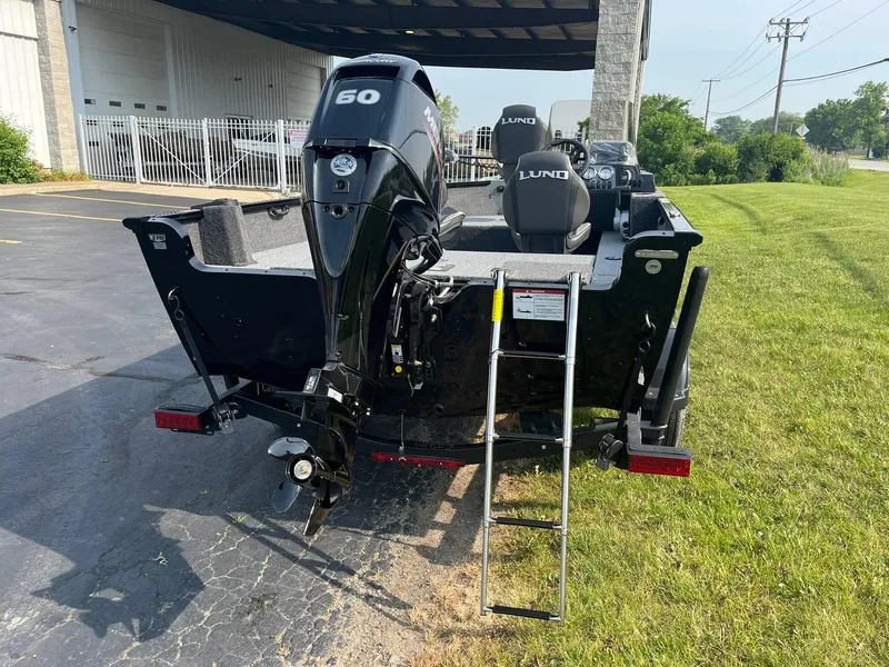 Slide: The Image of 2026 Lund 1650 Rebel XL SS boat with 60 HP motor and ladder, parked on grass. - 2