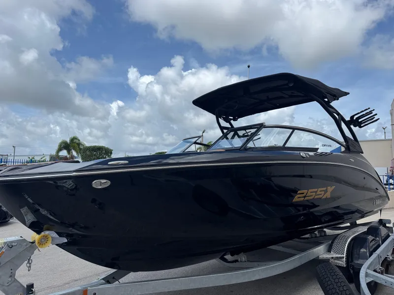 Slide: The Image of 2025 Yamaha Boats 255XD, sleek black design, on trailer under cloudy sky. - 2