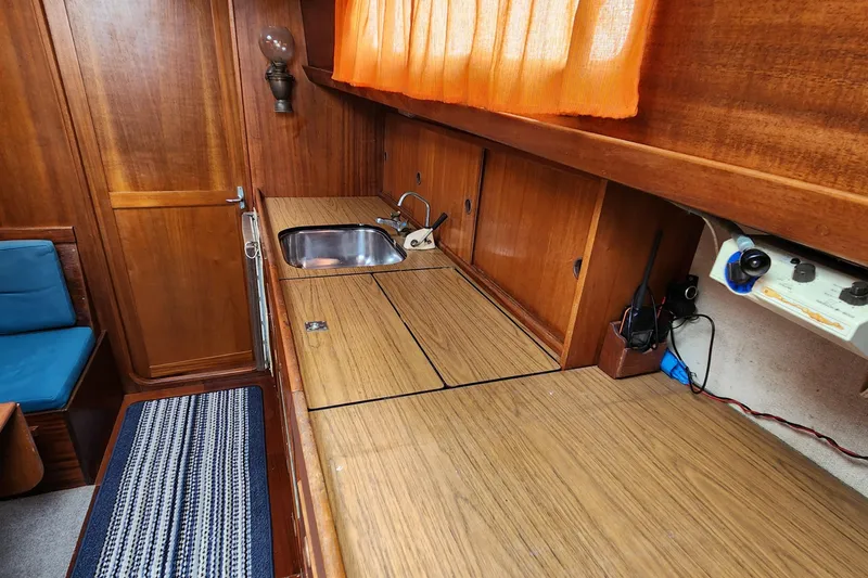 Slide: The Image of 1974 Hallberg-Rassy Rasmus 35 yacht interior with wooden cabinetry and compact kitchen area. - 38