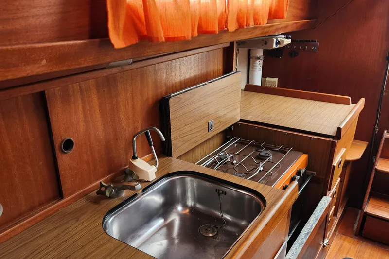 Slide: The Image of 1974 Hallberg-Rassy Rasmus 35 yacht interior kitchen with sink, stove, and wooden cabinetry. - 40
