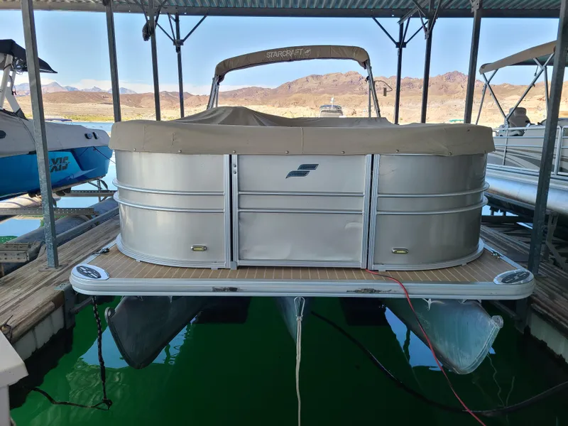 Slide: The Image of 2018 Starcraft 24 CXE Tritoon boat docked in a marina, covered and ready for use. - 14