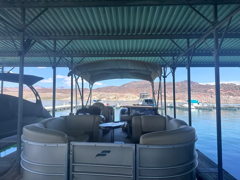 Slide: The Image of 2018 Starcraft 24 CXE Tritoon docked under a metal canopy on a sunny day. - 3