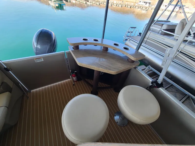 Slide: The Image of 2018 Starcraft 24 CXE Tritoon interior with seating and table on a calm lake. - 8