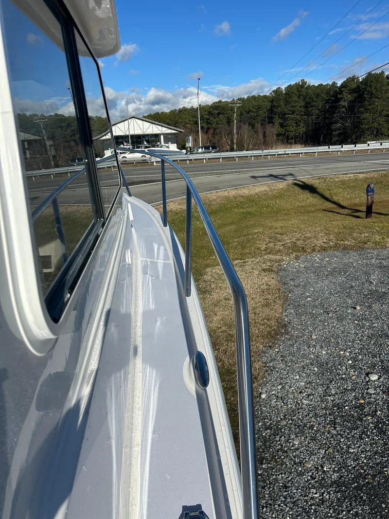 Slide: The Image of 2024 NorthCoast 255HT boat side view with railing, parked near road and trees. - 43