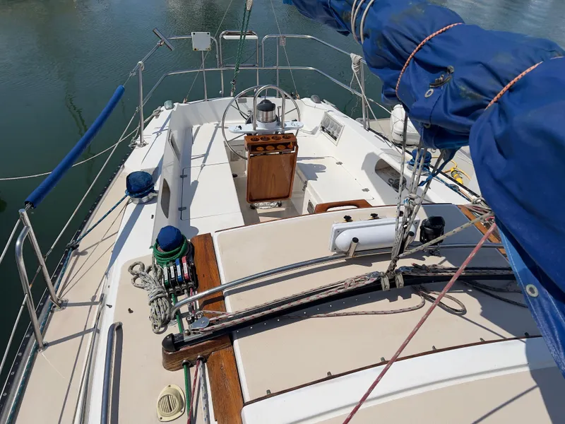 Slide: The Image of 1986 Catalina 30 sailboat deck with rigging and steering wheel, docked on calm water. - 7