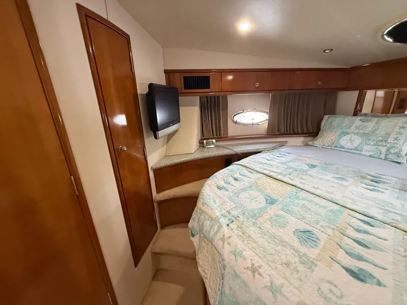 Slide: The Image of 2001 Carver 396 Motor Yacht bedroom with TV, wooden cabinets, and patterned bedding. - 44