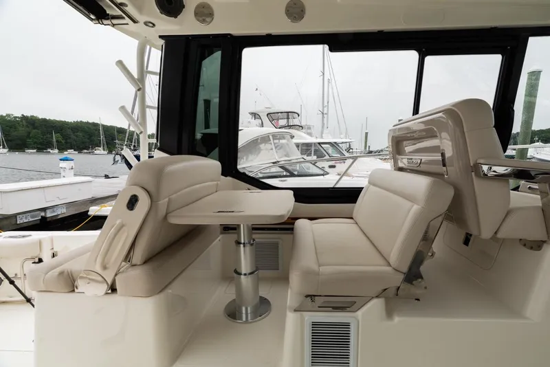 Slide: The Image of 2024 Boston Whaler 405 Conquest interior with plush seating and table, docked at marina. - 33