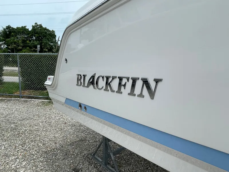 Slide: The Image of 2026 Blackfin 222CC boat side view with logo, parked on gravel. - 2