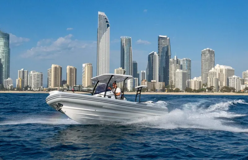 Slide: The Image of 2025 Grand Inflatables G750 boat cruising near a city skyline on a sunny day. - 10