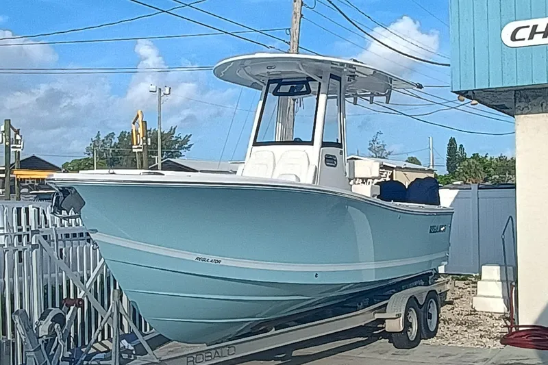 The Image of 2025 Regulator 23 Center Console boat on trailer, light blue hull, parked outdoors. - 0