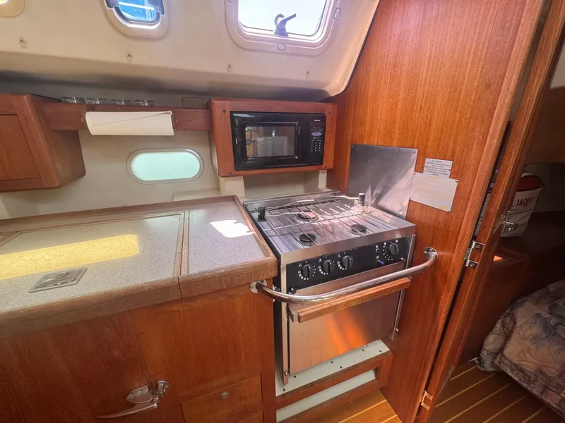 Slide: The Image of Compact kitchen in a 2000 Hunter 410 sailboat with stove, microwave, and wooden cabinetry. - 41