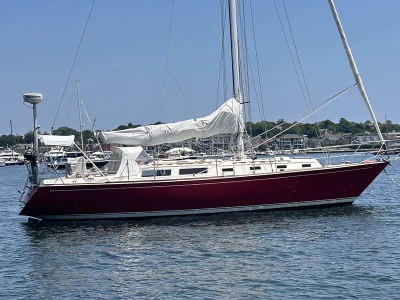 Slide: The Image of 1983 Sabre 38 sailboat with red hull and white sails on calm water. - 4