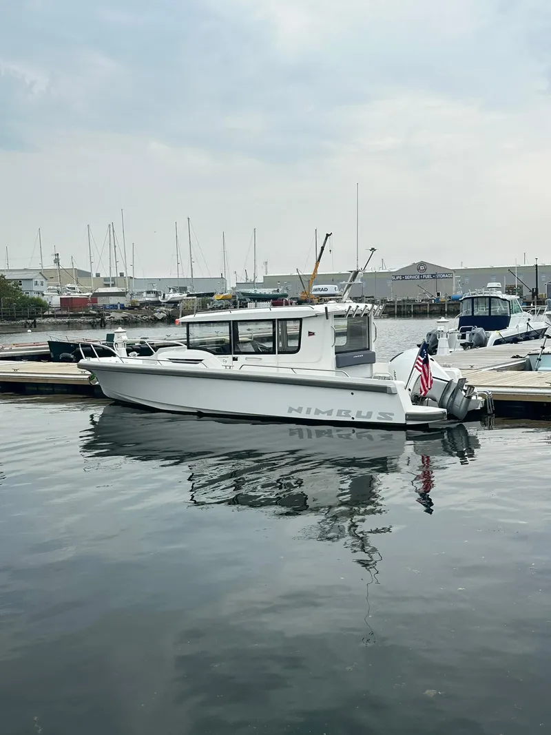 Slide: The Image of 2023 Nimbus Commuter 9 boat docked in a marina, calm water, overcast sky. - 10