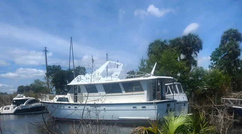 Slide: The Image of 1982 Hatteras 61 Motor Yacht docked near lush greenery under a clear blue sky. - 2