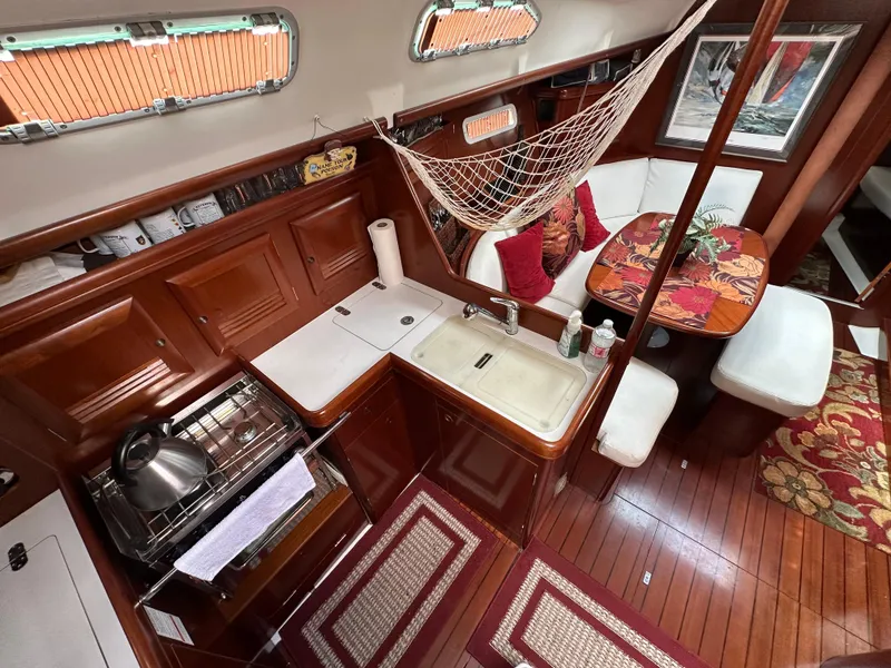 Slide: The Image of Interior of 2004 Beneteau 393 yacht with kitchen and dining area, featuring wood finish and cozy decor. - 32