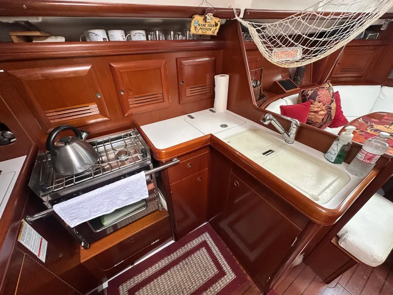 Slide: The Image of 2004 Beneteau 393 yacht kitchen with wooden cabinetry, stove, sink, and cozy seating area. - 52