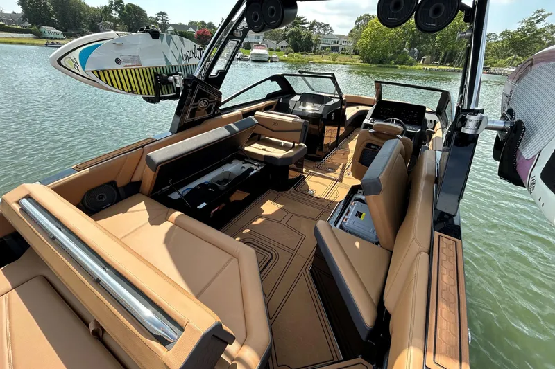 Slide: The Image of 2026 Cobalt R8 Surf boat interior with tan seating and surfboard rack on a lake. - 17