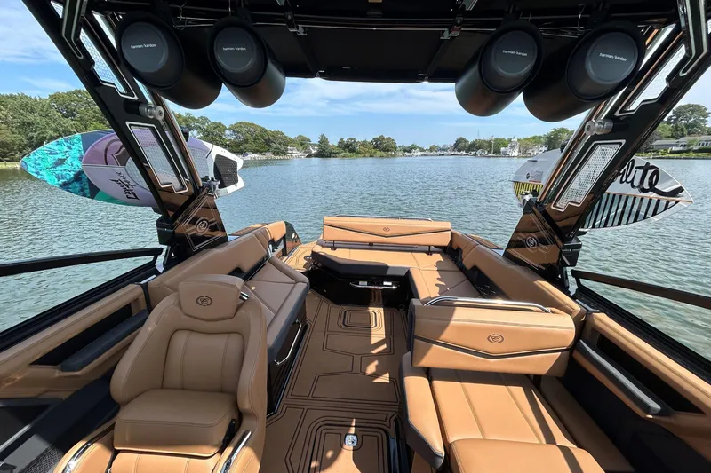 Slide: The Image of 2026 Cobalt R8 Surf boat interior with tan seating, wakeboards, and speakers on a calm lake. - 24