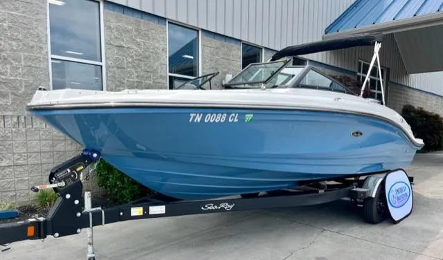 Slide: The Image of 2023 Sea Ray SPX 210 OB boat on trailer, blue hull, parked outside building. - 2