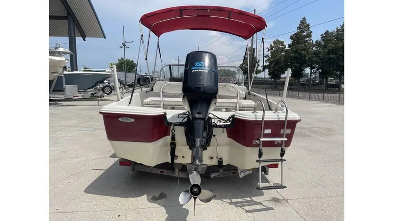 Slide: The Image of 2002 Bay Stealth 1880 boat with red canopy and outboard motor, parked on concrete. - 3