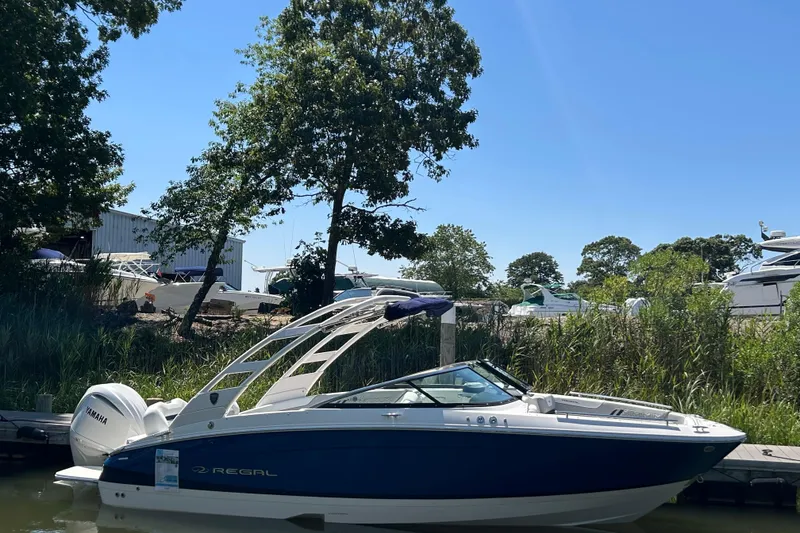 Slide: The Image of 2026 Regal LX4 boat docked by lush greenery under clear blue sky. - 2
