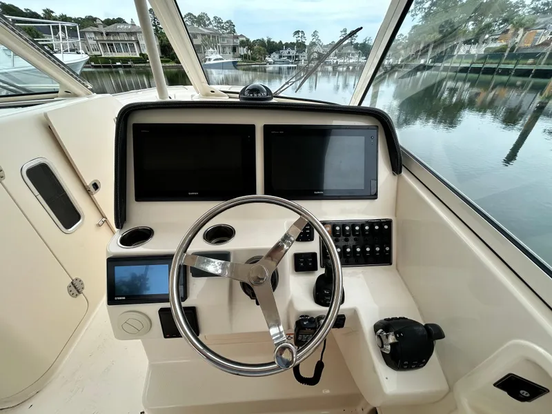 Slide: The Image of 2018 Grady-White Freedom 325 boat helm with dual screens and steering wheel, docked by calm waters. - 14