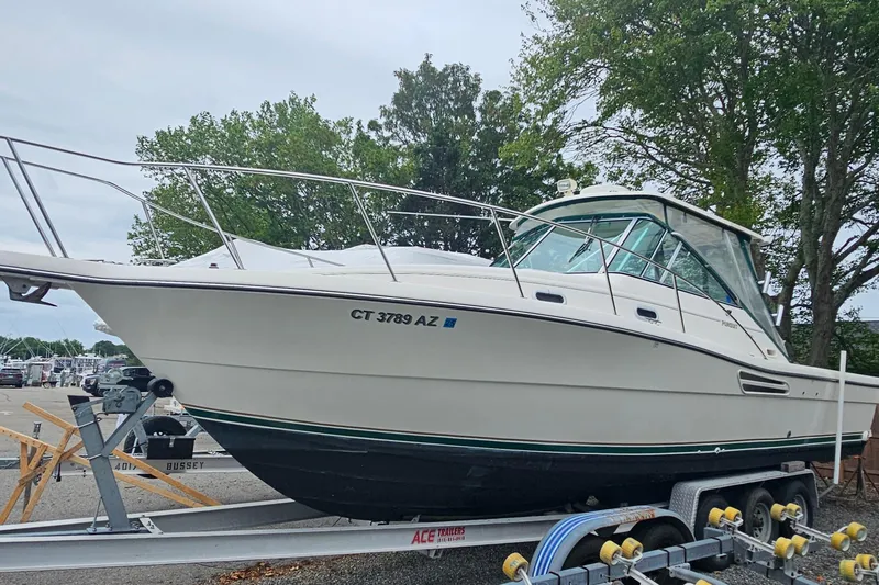 Slide: The Image of 2000 Pursuit 3000 Express boat on trailer, parked near trees. - 1