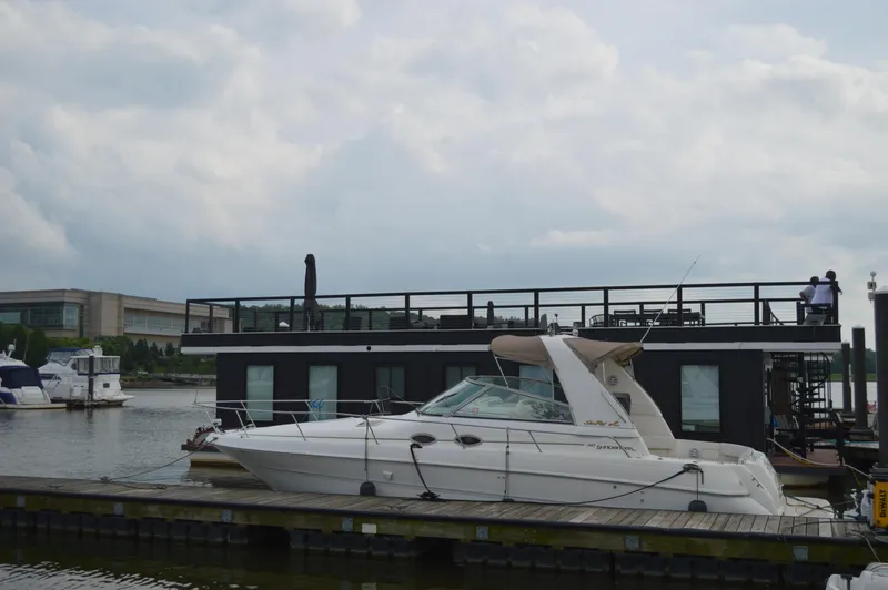 Slide: The Image of 1998 Sea Ray 310 Sundancer docked beside a modern houseboat on a cloudy day. - 13