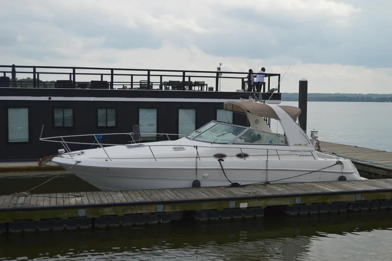 Slide: The Image of 1998 Sea Ray 310 Sundancer docked beside a houseboat on a cloudy day. - 14