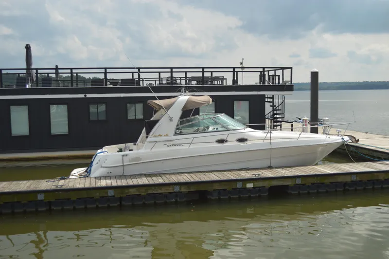 Slide: The Image of 1998 Sea Ray 310 Sundancer docked beside a houseboat on a cloudy day. - 8