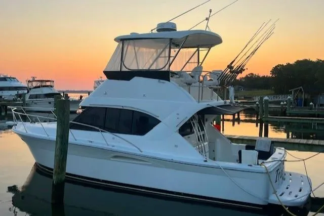 The Image of 2003 Riviera 350 yacht docked at sunset, featuring fishing rods and calm waters. - 0
