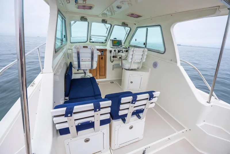 Slide: The Image of 2005 Back Cove Downeast Hardtop boat interior with seating and helm, on calm water. - 24