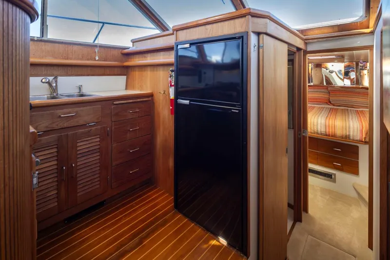 Slide: The Image of 1993 Tollycraft 40 Sport Sedan interior with wood cabinetry, black fridge, and cozy bedroom. - 18