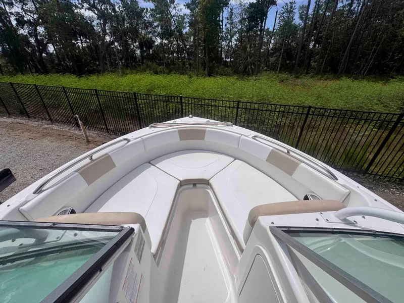 Slide: The Image of 2019 Robalo R227 Dual Console boat interior with seating, surrounded by greenery and fence. - 11