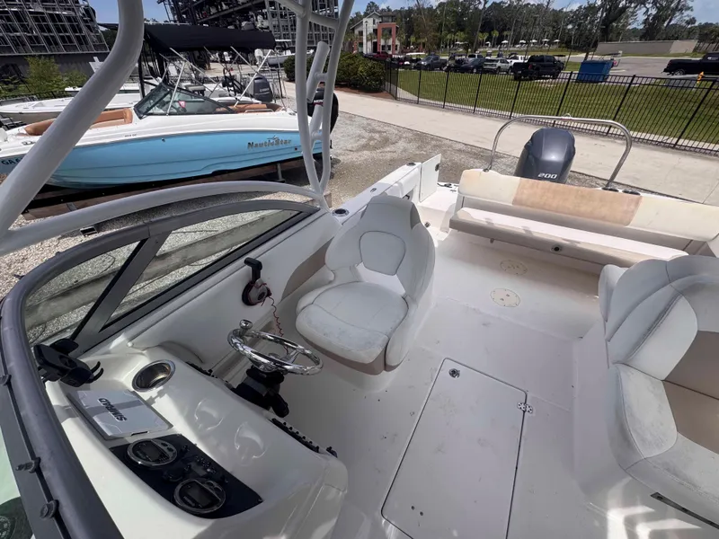 Slide: The Image of 2019 Robalo R227 Dual Console boat with spacious seating, parked near a fence and greenery. - 27