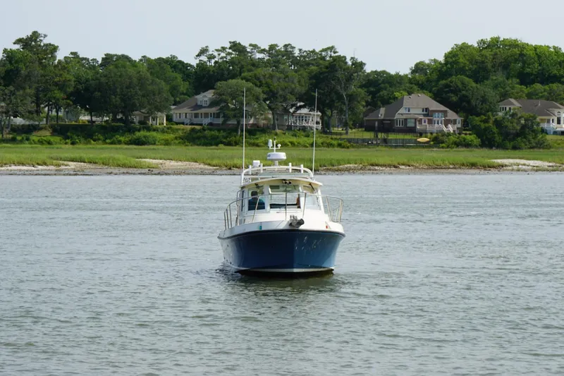 Slide: The Image of 1996 Albin 28TE boat cruising on a calm river with houses and trees in the background. - 2