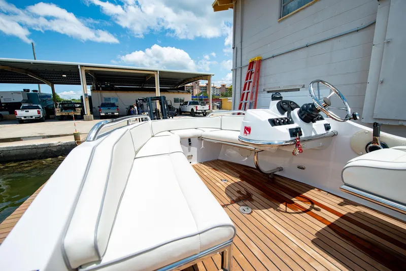 Slide: The Image of 2006 Novurania RHIB boat with white seating and wooden deck, docked near a warehouse. - 13