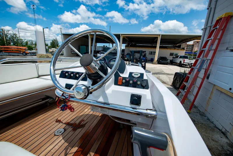 Slide: The Image of 2006 Novurania RHIB boat interior with steering wheel, wooden deck, and control panel under blue sky. - 21